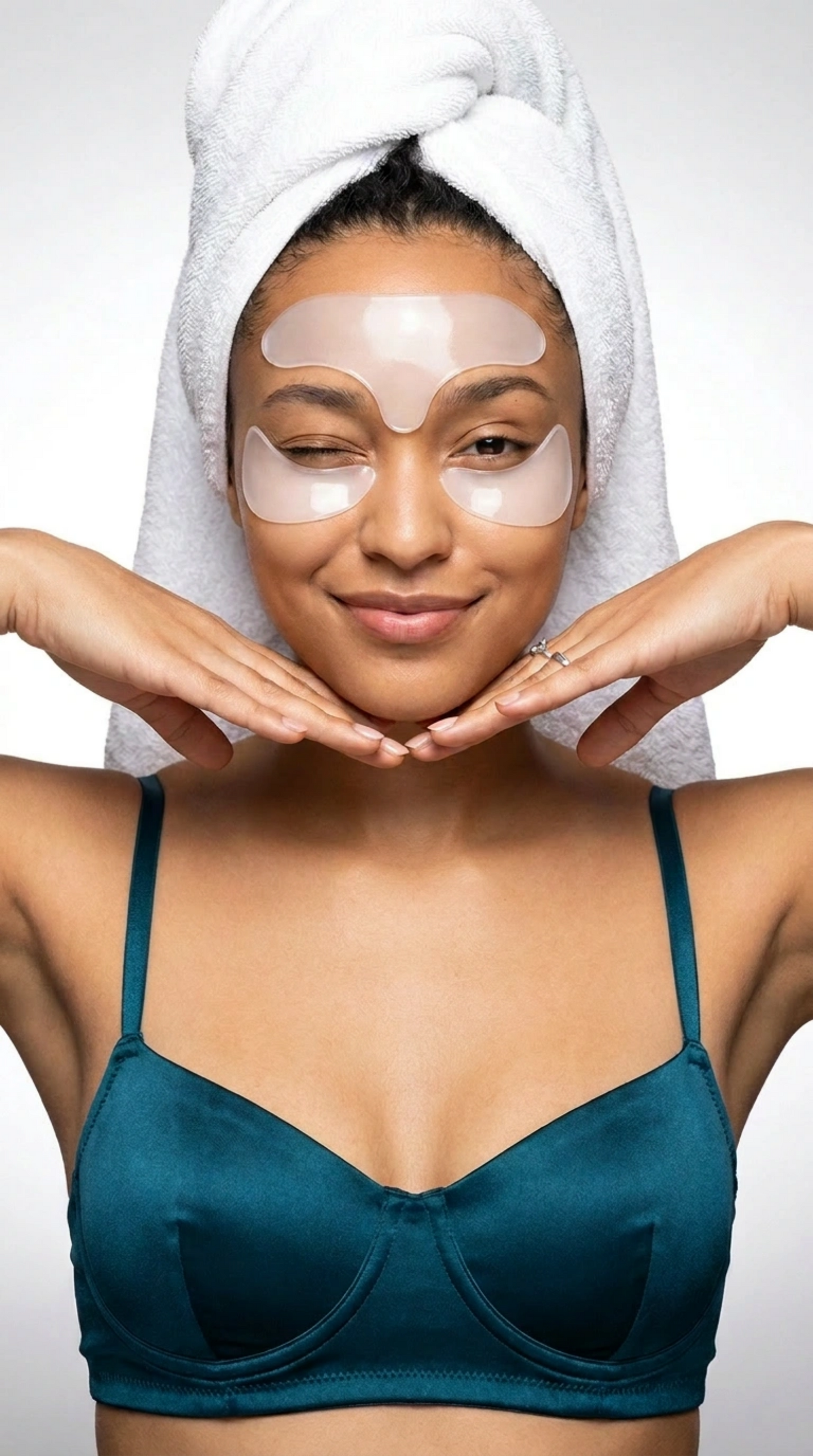 Woman wearing eye masks with a towel on her head, against a plain background