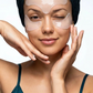 Woman with under-eye patches and a towel on her head against a white background